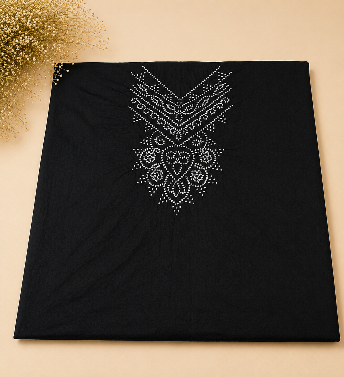 A black rectangular fabric item, likely a scarf or shawl, laid flat on a beige background with a decorative gold floral arrangement in the top-left corner. The fabric features a prominent white rhinestone or bead geometric and floral mandala pattern printed or embroidered in the upper half.