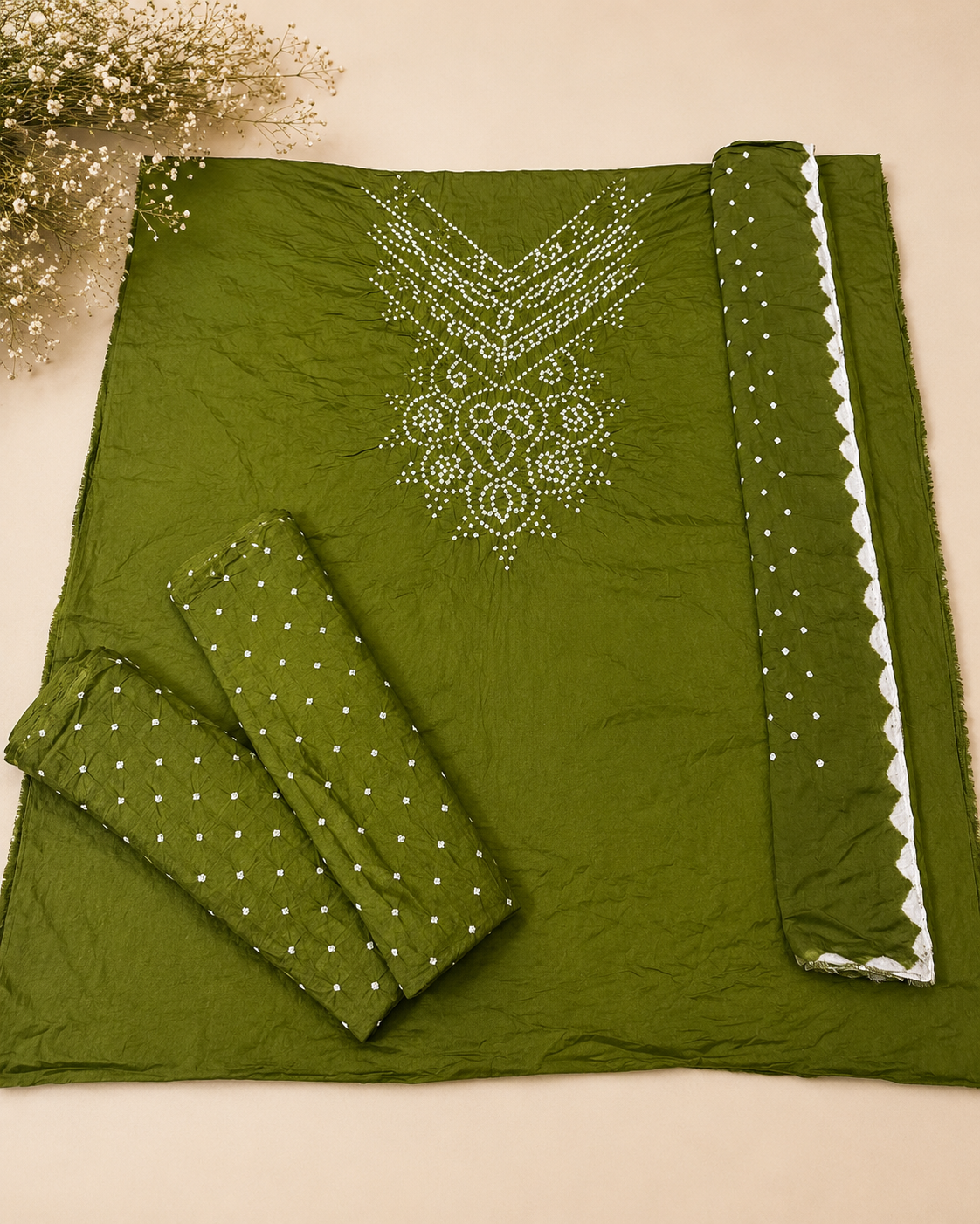An olive green fabric set with white dot patterns and white embroidered details, laid out on a beige background with a decorative floral corner.