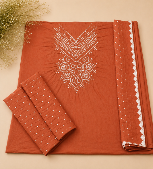 Terracotta orange unstitched salwar suit material set featuring a kurta fabric with white printed embroidery, matching trousers, and a border fabric with a scalloped white edge, displayed on a beige background with dried flowers.