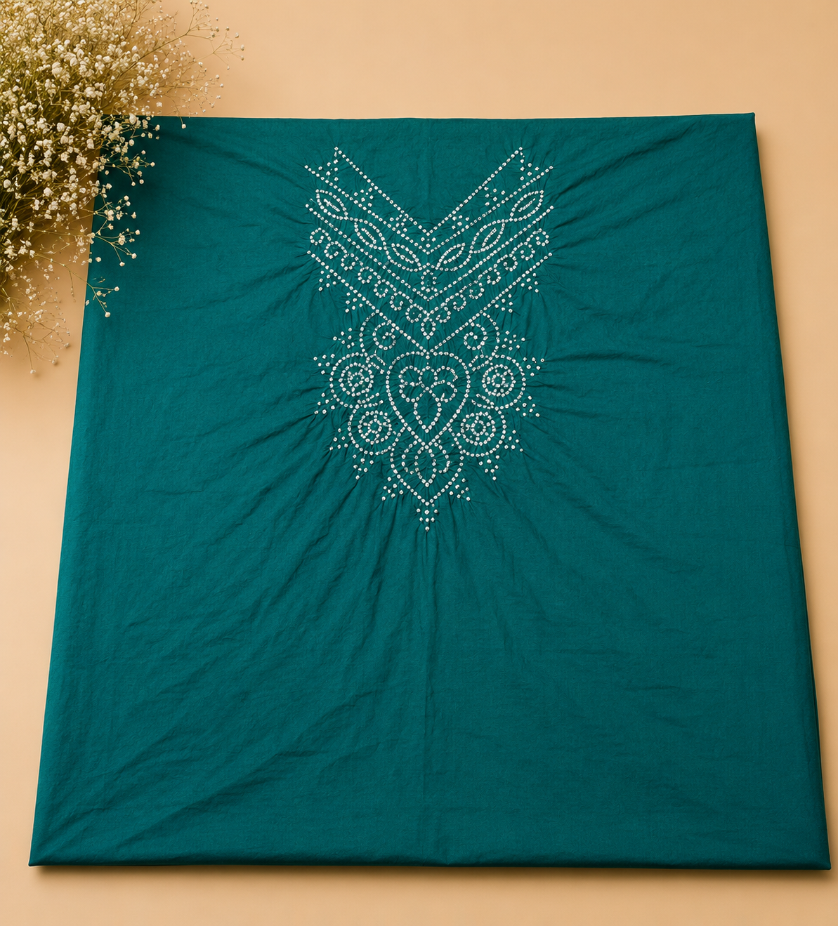 A teal green fabric item, likely a scarf, shawl, or sari, featuring a white embroidered mandala pattern on the front, displayed flat against a warm beige background with small white flowers in the top-left corner.
