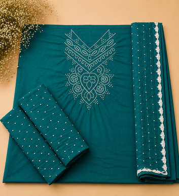A folded teal fabric set with white embroidered patterns and dotted borders, arranged on a beige background with decorative dried flowers in the corner.
