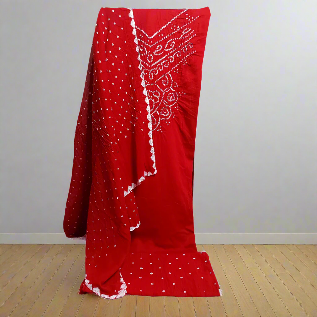 Red Bandhani suit fabric with draped over a chair against a plain wall.