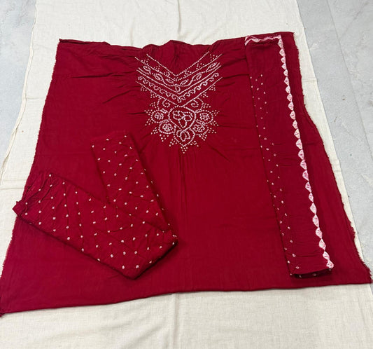 A folded deep red salwar suit set laid flat on a white fabric background, featuring white embroidered patterns on the chest, white polka dots on the fabric, and a white scalloped border on the dupatta.