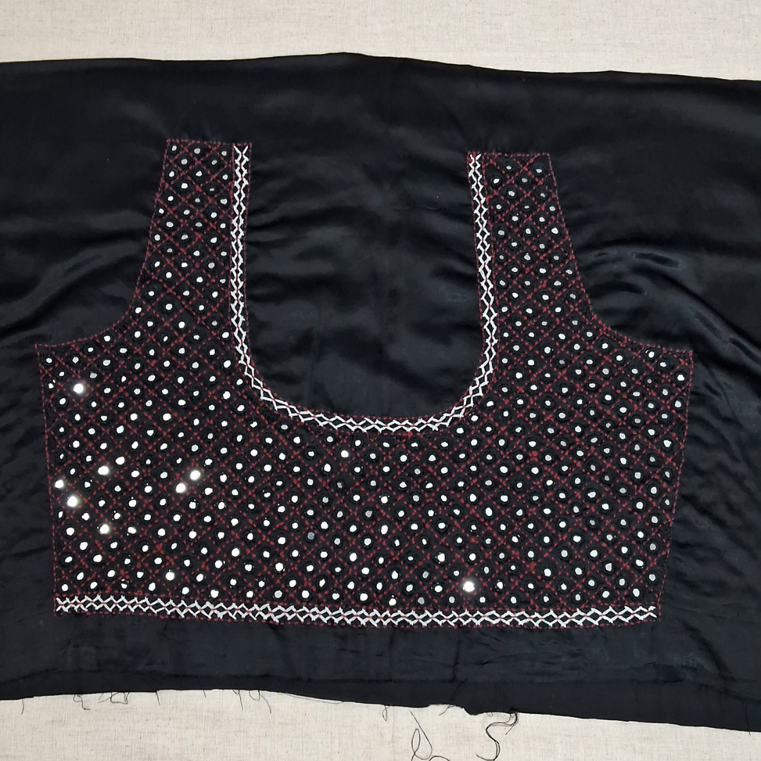 Black fabric blouse piece with mirror work embellishments and white zigzag border stitching, laid flat on a light beige surface.