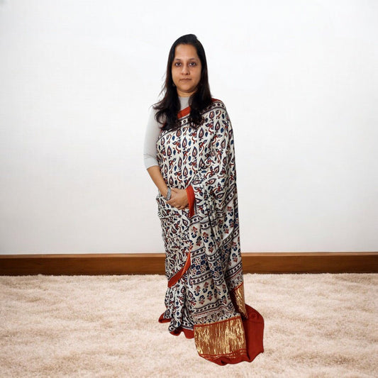 Woman wearing a ajrakh saree standing on a carpeted floor with a white wall background