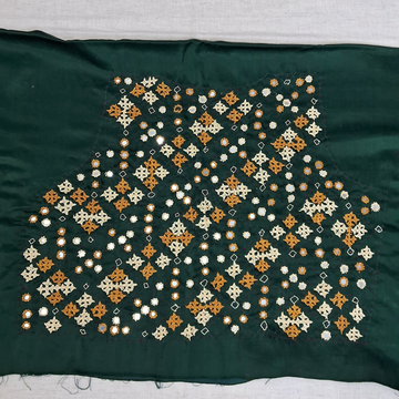 A dark green fabric garment piece featuring an intricate hand-embroidered pattern of small flowers and geometric motifs in orange, cream, and white, laid flat on a light gray surface.