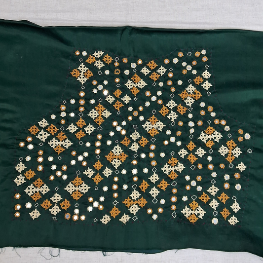 A dark green fabric garment piece featuring an intricate hand-embroidered pattern of small flowers and geometric motifs in orange, cream, and white, laid flat on a light gray surface.