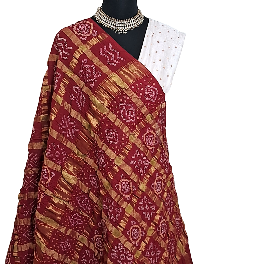 close up of red gharchola bandhani  saree pallu with a white blouse on a mannequin against a white background