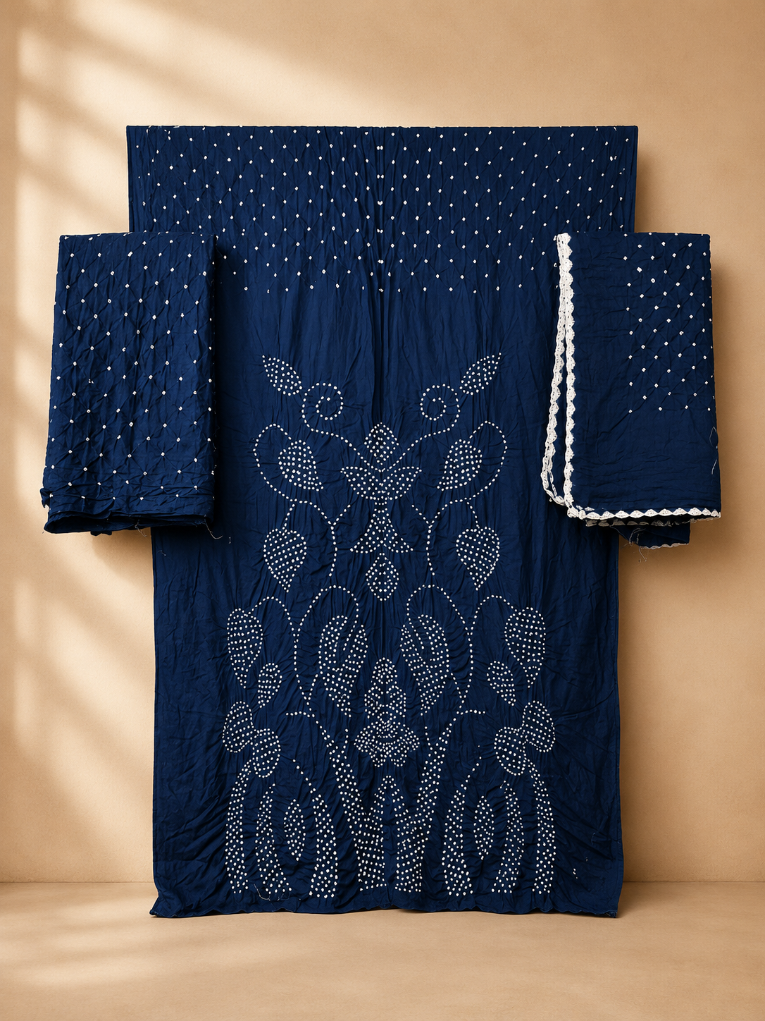 A indigo blue traditional outfit set with intricate white embroidery and dotted patterns, displayed against a warm beige background with soft shadow overlays.