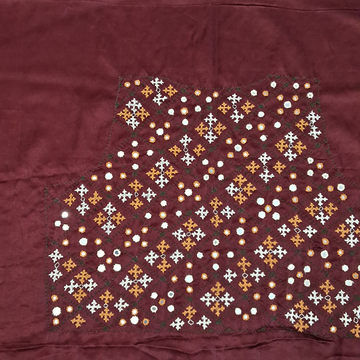A close-up of a maroon fabric panel featuring a detailed geometric and floral embroidered pattern in white, orange, and green.