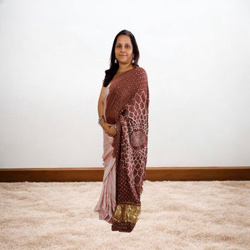 Woman wearing a bandhani saree standing on a carpeted floor with a white wall background