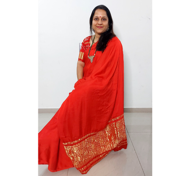 Woman wearing a modal silk red saree with gold border against a white background