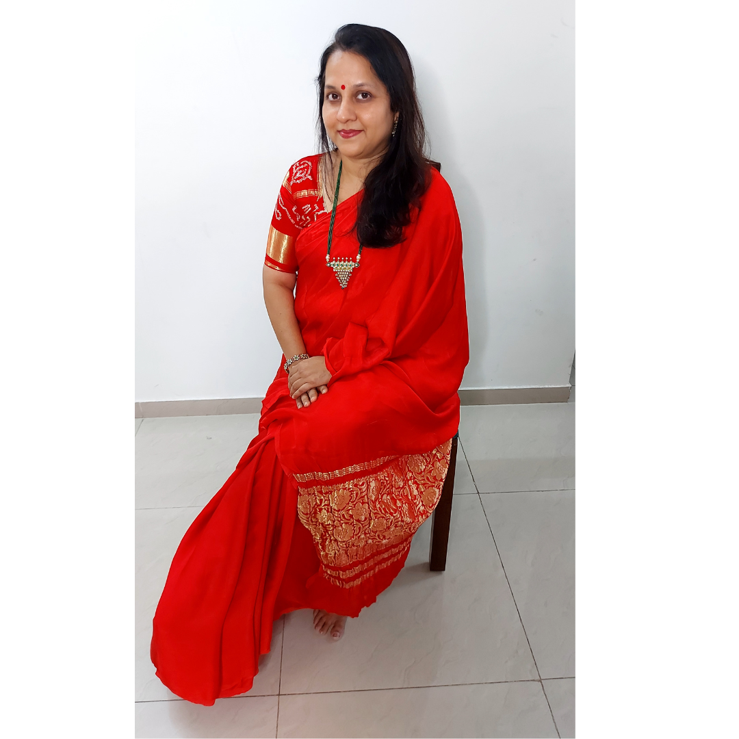 Woman in a modal silk plain red saree sitting on a chair against a white wall.