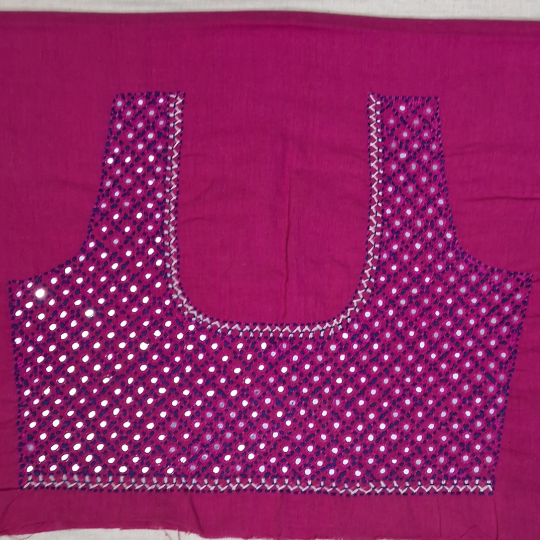A magenta pink blouse piece with a U-neckline, heavily decorated with silver mirror work and sequins in a dotted pattern, laid flat on a white surface.