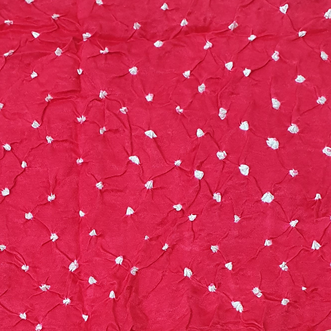 close up of white dana bandhej on tomato red pure gajji silk fabric