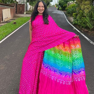 Woman in a bright pink and rainbow patterned saree standing on a road.