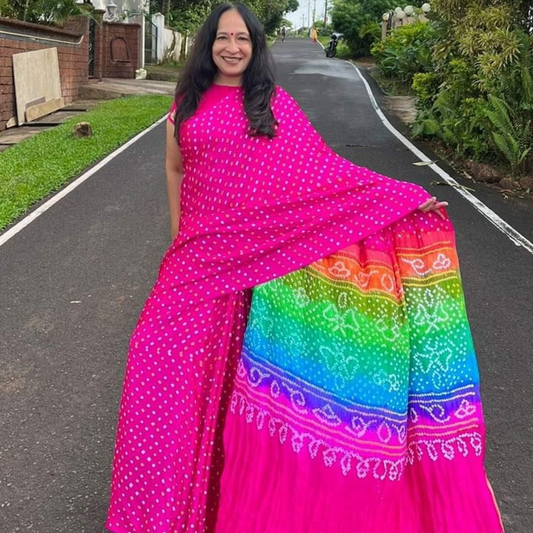Woman in a bright pink and rainbow patterned saree standing on a road.