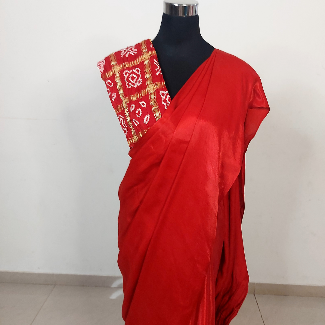 Red saree with a gharchola bandhani blouse piece on a mannequin against a white background
