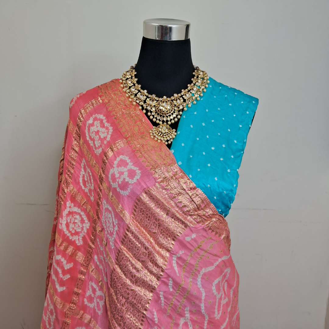 Mannequin wearing a pink Gharchola Bandhani saree with gold patterns and a blue blouse piece. 
